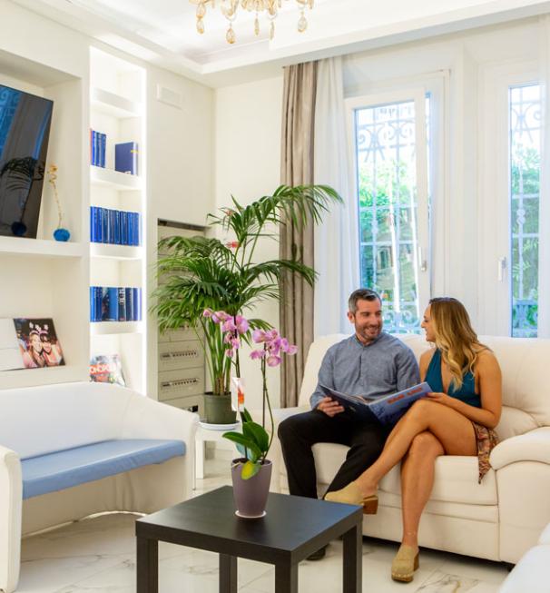Coppia seduta in salotto moderno con libri, TV e piante.