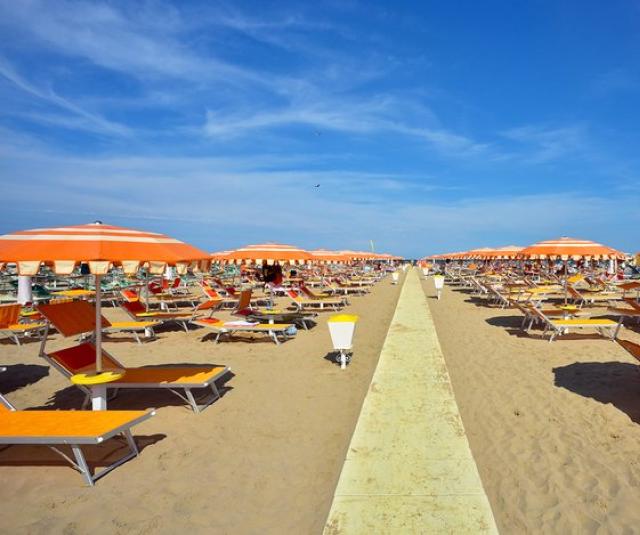 Sunny beach with orange umbrellas, loungers, and clear blue sky.