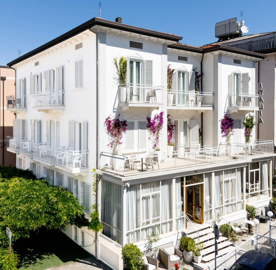 Hotel bianco con balconi e piante rampicanti in una strada tranquilla.